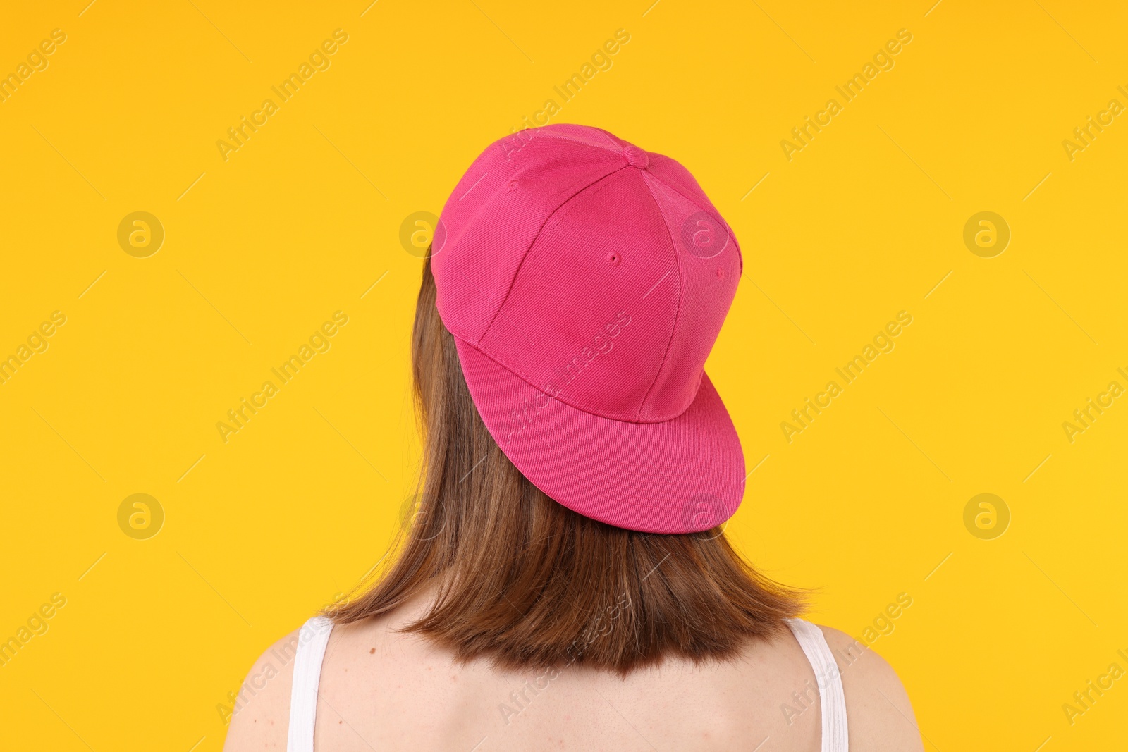 Photo of Young woman wearing stylish pink baseball hat on yellow background, back view