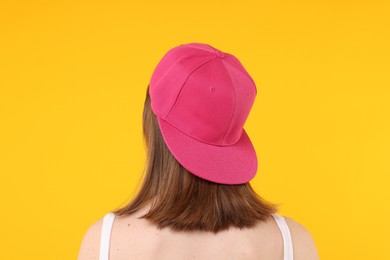 Photo of Young woman wearing stylish pink baseball hat on yellow background, back view