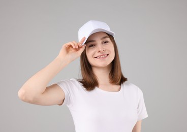 Photo of Young woman wearing stylish white baseball hat on light grey background