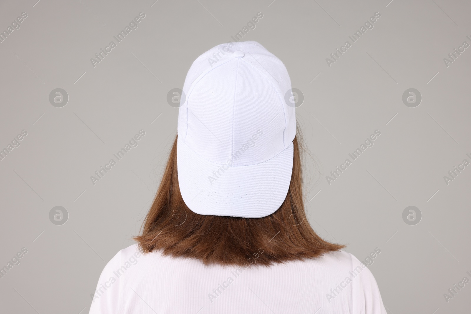 Photo of Young woman wearing stylish white baseball hat on light grey background, back view