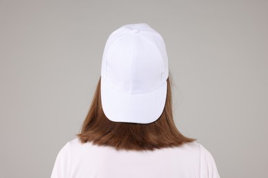 Photo of Young woman wearing stylish white baseball hat on light grey background, back view