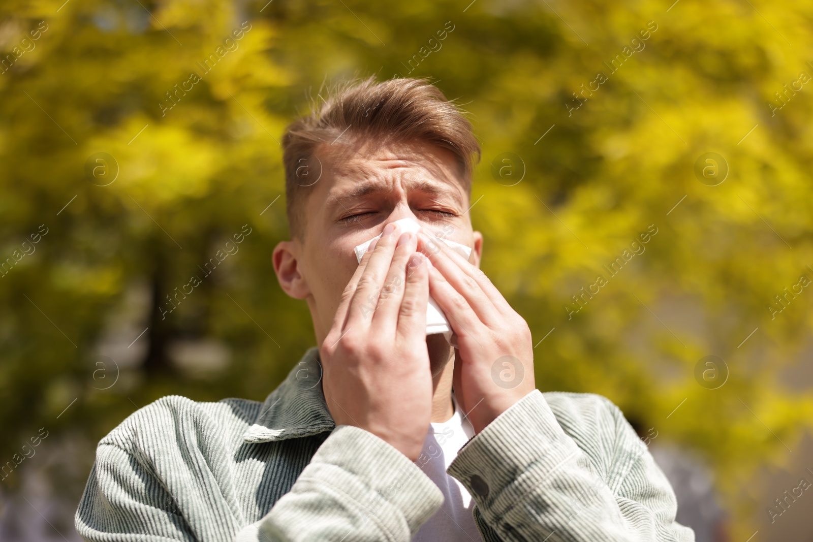Young man with paper tissue suffering from seasonal pollen allergy near tree on spring day Photo of Young man with paper tissue suffering from seasonal pollen allergy near tree on spring day