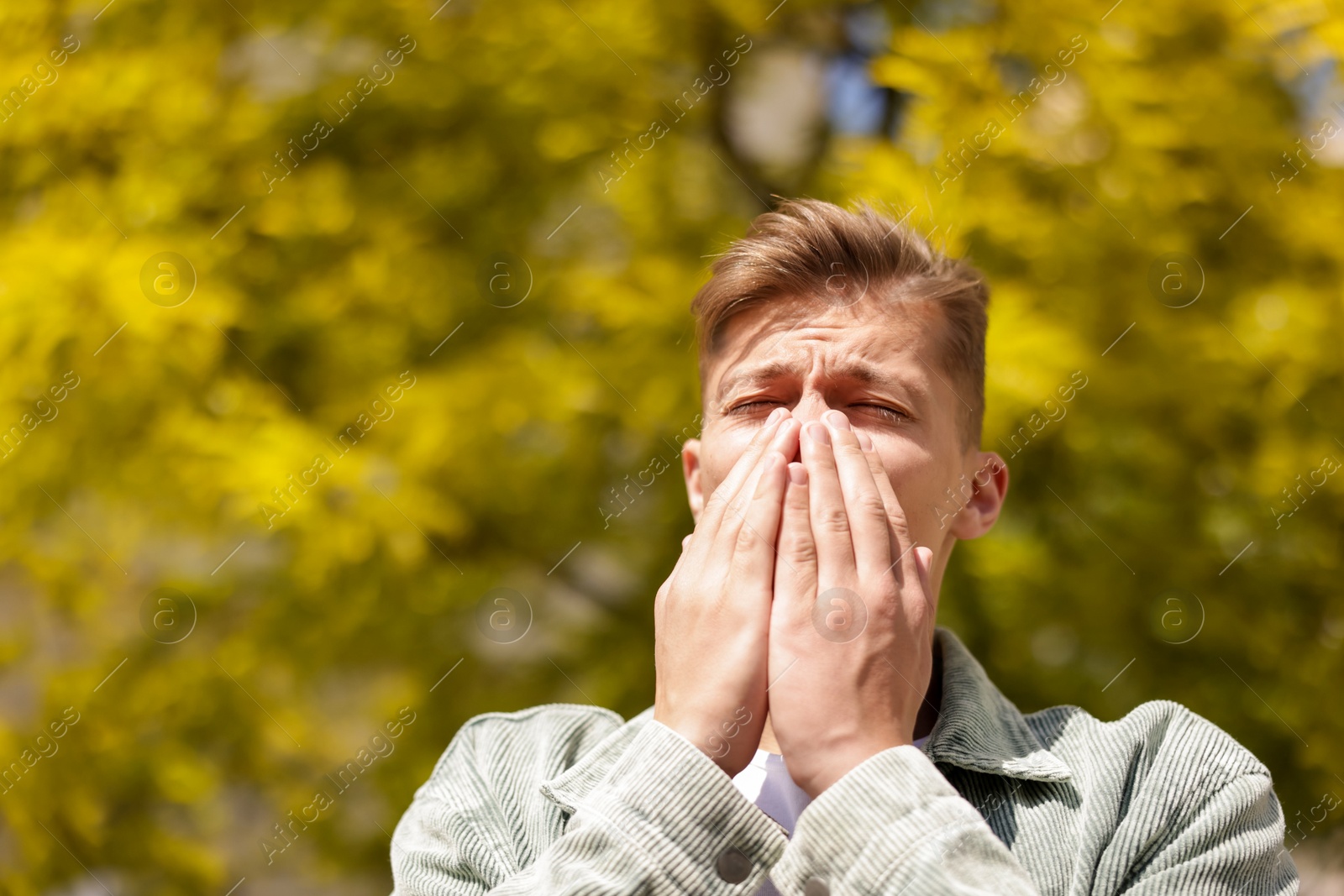 Young man suffering from seasonal pollen allergy near tree on spring day. Space for text Photo of Young man suffering from seasonal pollen allergy near tree on spring day. Space for text