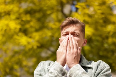Photo of Young man suffering from seasonal pollen allergy near tree on spring day. Space for text