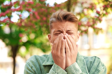 Photo of Young man suffering from seasonal pollen allergy near blossoming tree on spring day