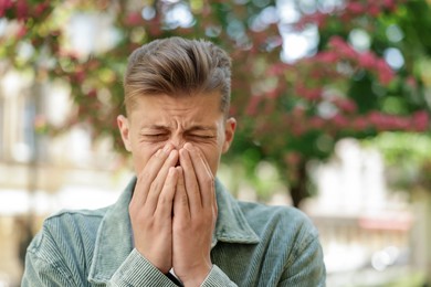 Photo of Young man suffering from seasonal pollen allergy near blossoming tree on spring day. Space for text