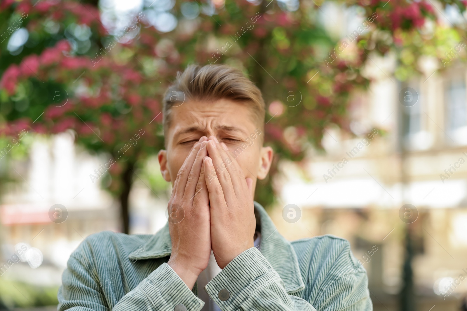 Young man suffering from seasonal pollen allergy near blossoming tree on spring day Photo of Young man suffering from seasonal pollen allergy near blossoming tree on spring day