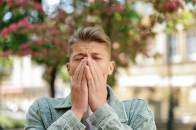 Photo of Young man suffering from seasonal pollen allergy near blossoming tree on spring day