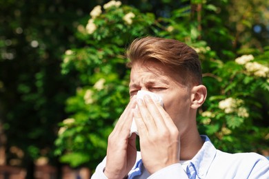 Photo of Young man with paper tissue suffering from seasonal pollen allergy near blossoming tree on spring day. Space for text