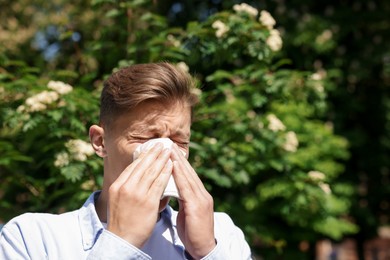 Photo of Young man with paper tissue suffering from seasonal pollen allergy near blossoming tree on spring day. Space for text