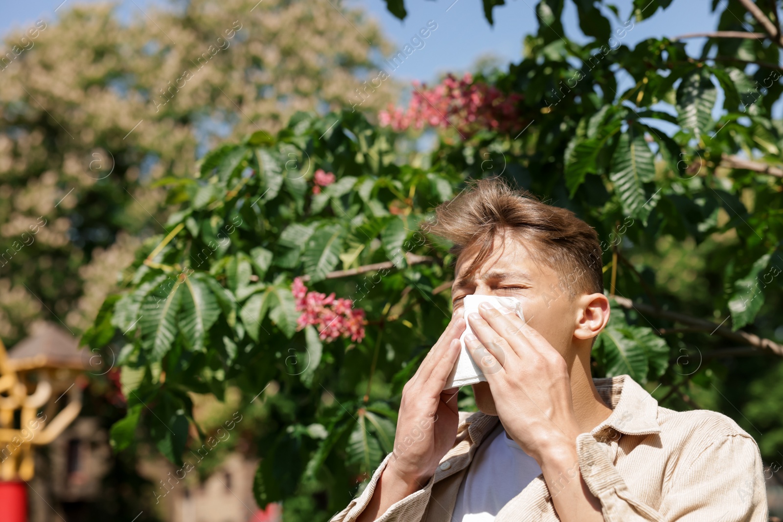 Photo of Young man with paper tissue suffering from seasonal pollen allergy near blossoming tree on spring day. Space for text