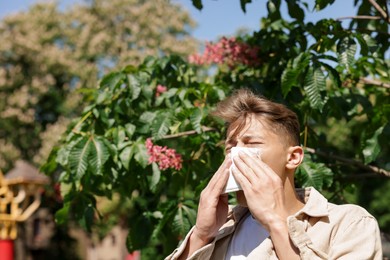 Photo of Young man with paper tissue suffering from seasonal pollen allergy near blossoming tree on spring day. Space for text