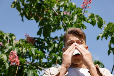 Photo of Young man with paper tissue suffering from seasonal pollen allergy near blossoming tree on spring day. Space for text
