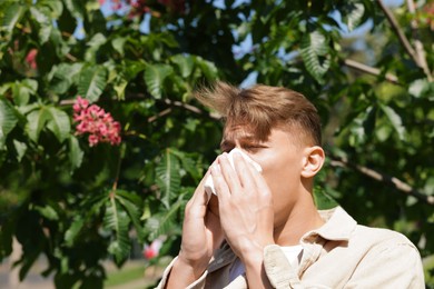Photo of Young man with paper tissue suffering from seasonal pollen allergy near blossoming tree on spring day. Space for text