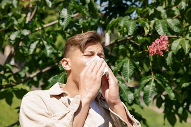 Photo of Young man with paper tissue suffering from seasonal pollen allergy near blossoming tree on spring day. Space for text