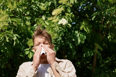 Photo of Young man with paper tissue suffering from seasonal pollen allergy near blossoming tree on spring day. Space for text