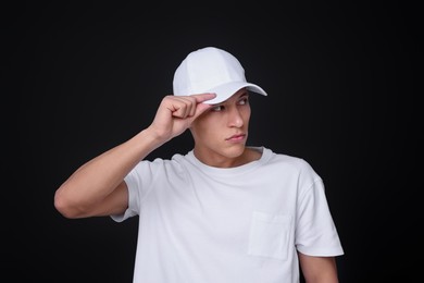 Photo of Young man wearing stylish white baseball hat on black background