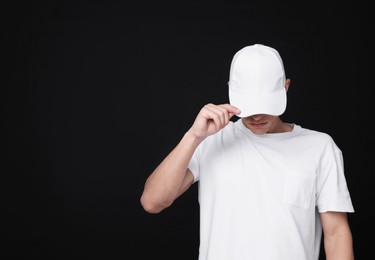 Photo of Young man wearing stylish white baseball hat on black background, space for text