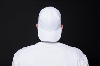 Photo of Young man wearing stylish white baseball hat on black background, back view