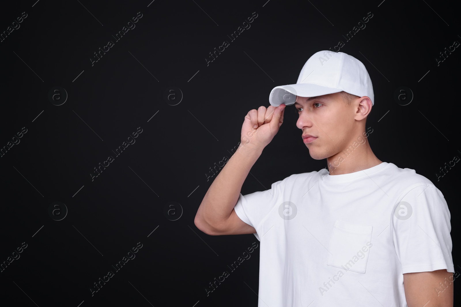 Photo of Young man wearing stylish white baseball hat on black background, space for text