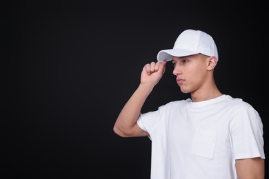 Photo of Young man wearing stylish white baseball hat on black background, space for text