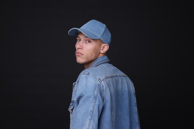 Photo of Young man wearing stylish denim baseball hat on black background