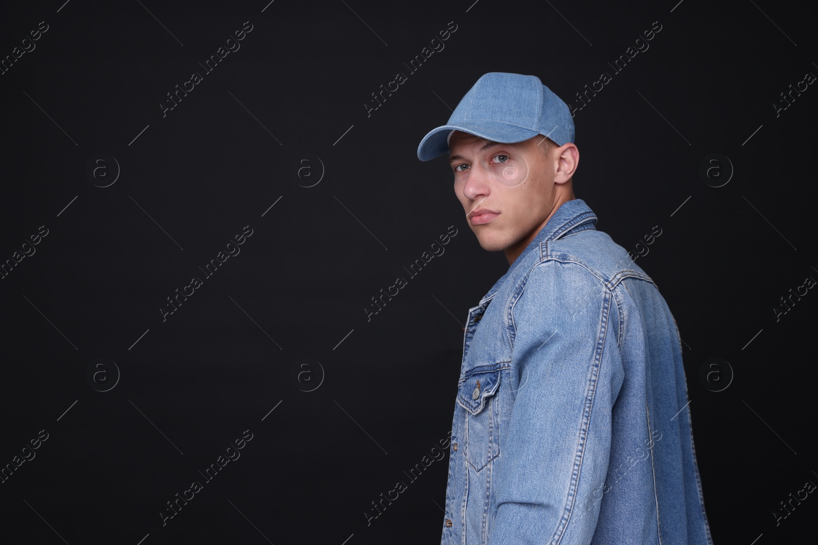 Photo of Young man wearing stylish denim baseball hat on black background, space for text