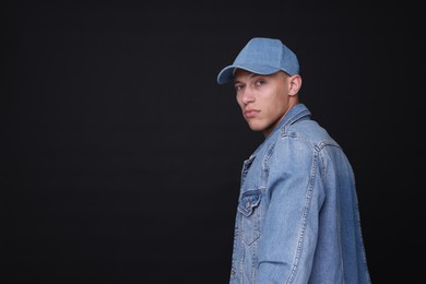 Photo of Young man wearing stylish denim baseball hat on black background, space for text