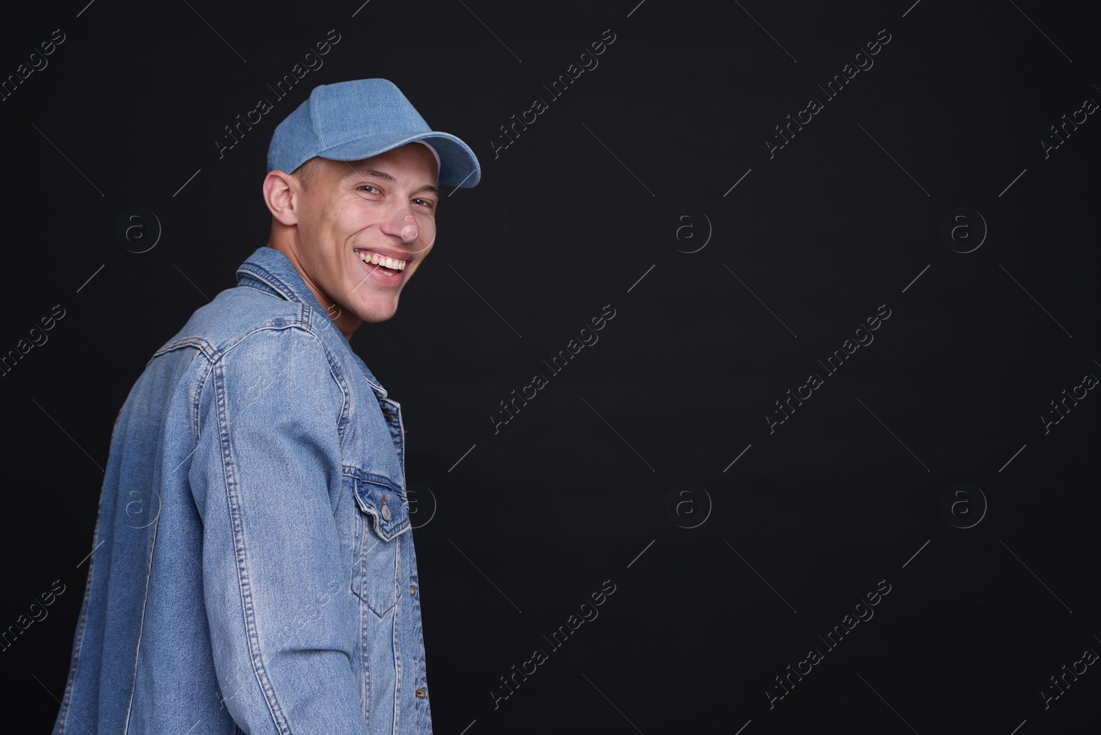 Photo of Young man wearing stylish denim baseball hat on black background, space for text