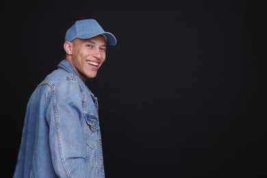 Photo of Young man wearing stylish denim baseball hat on black background, space for text