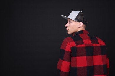 Photo of Young man wearing stylish baseball hat on black background, space for text