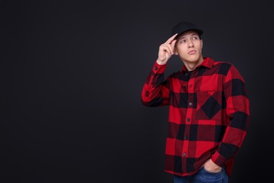 Photo of Young man wearing stylish baseball hat on black background, space for text