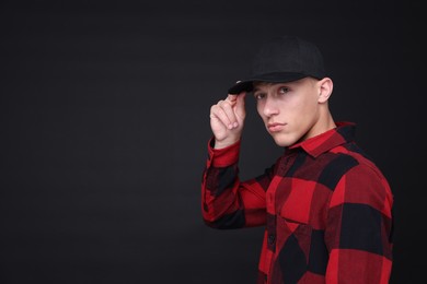 Photo of Young man wearing stylish baseball hat on black background, space for text