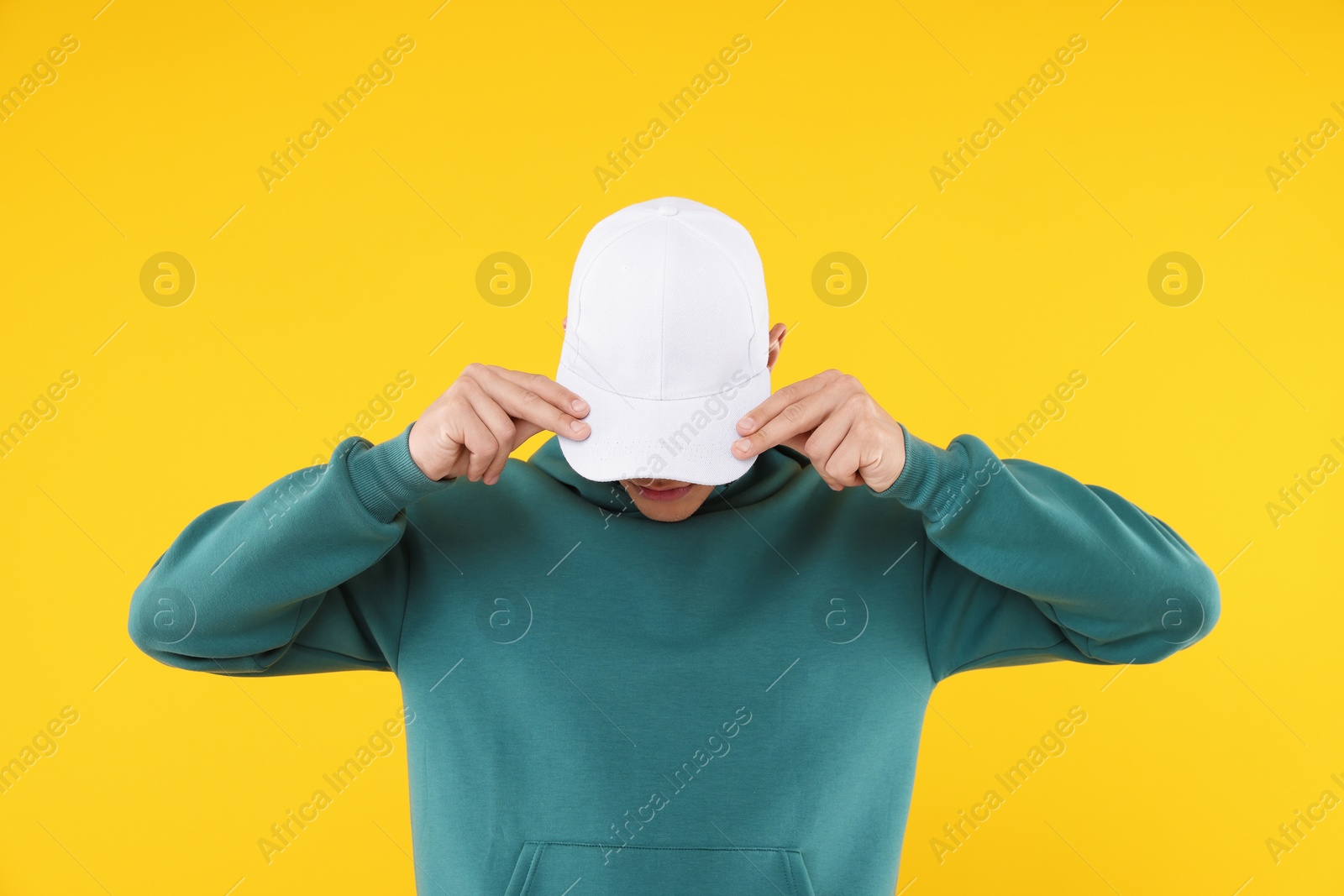 Young man wearing stylish white baseball hat on yellow background Photo of Young man wearing stylish white baseball hat on yellow background