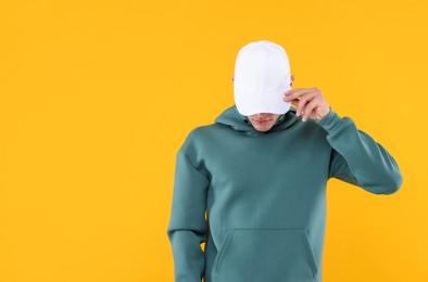 Photo of Young man wearing stylish white baseball hat on yellow background, space for text