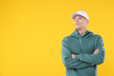 Photo of Young man wearing stylish white baseball hat on yellow background, space for text