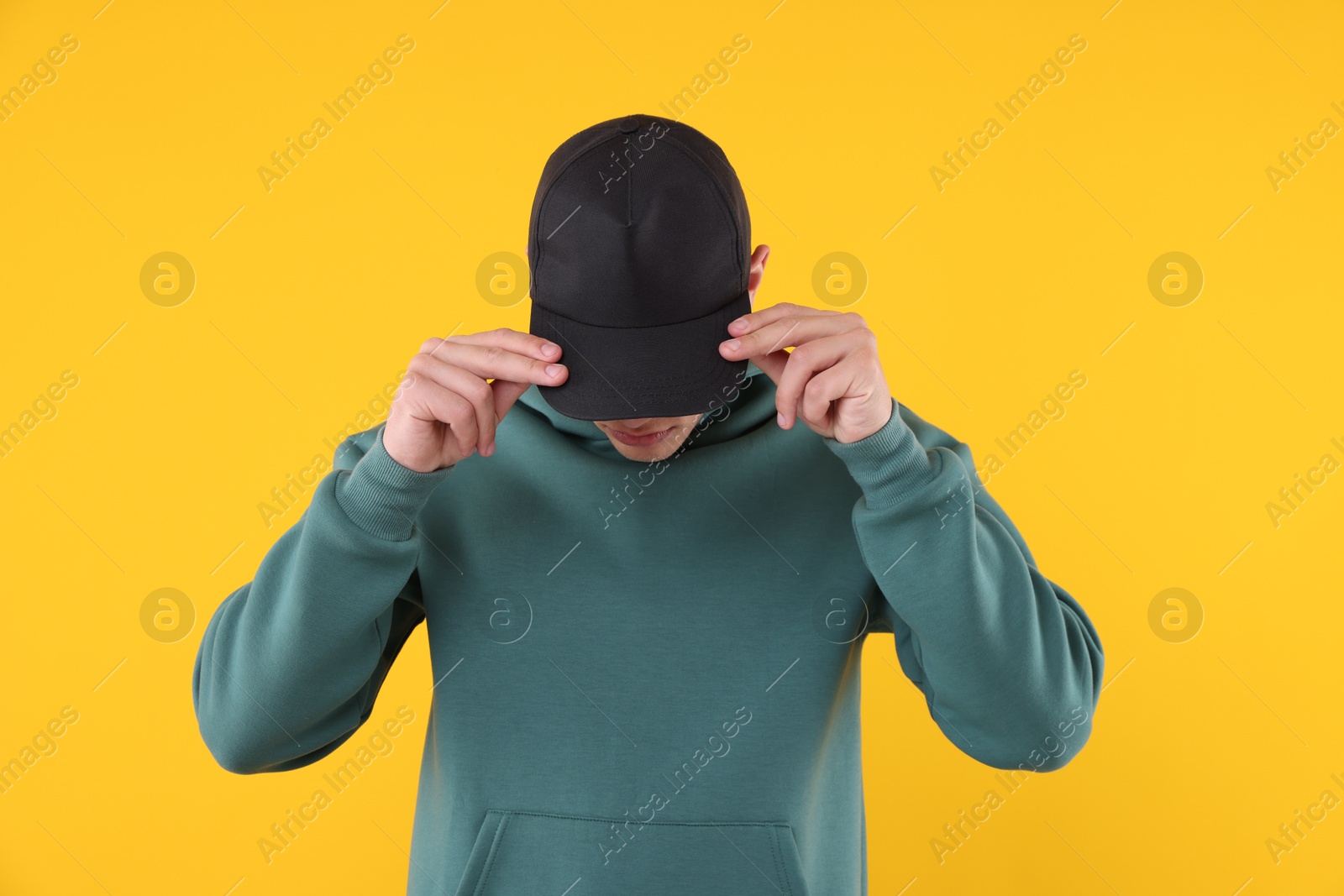 Young man wearing stylish black baseball hat on yellow background Photo of Young man wearing stylish black baseball hat on yellow background