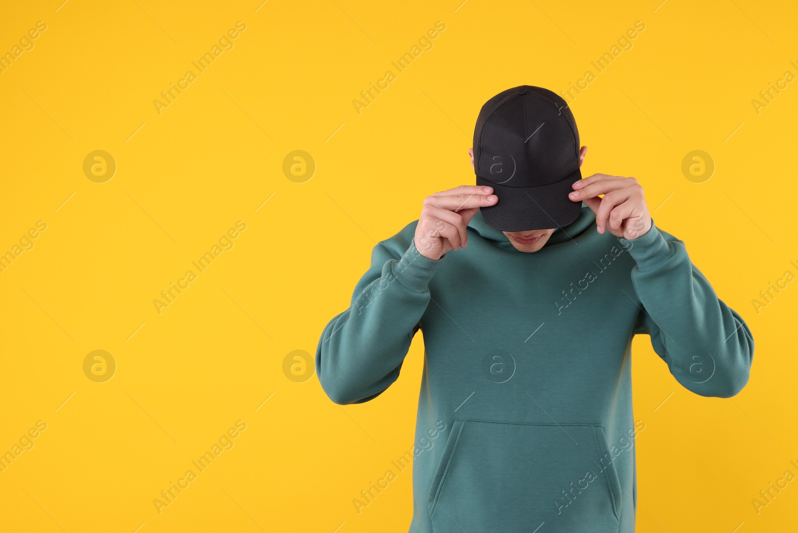 Young man wearing stylish black baseball hat on yellow background, space for text Photo of Young man wearing stylish black baseball hat on yellow background, space for text
