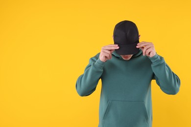 Photo of Young man wearing stylish black baseball hat on yellow background, space for text