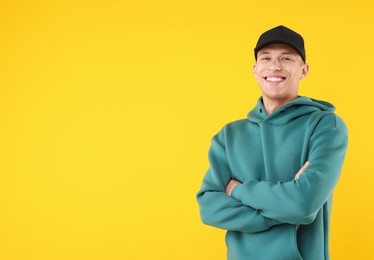Photo of Young man wearing stylish black baseball hat on yellow background, space for text