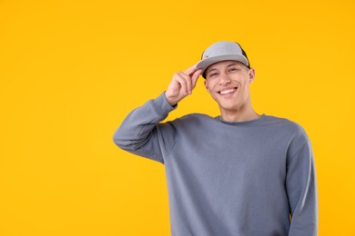 Photo of Young man wearing stylish baseball hat on yellow background, space for text