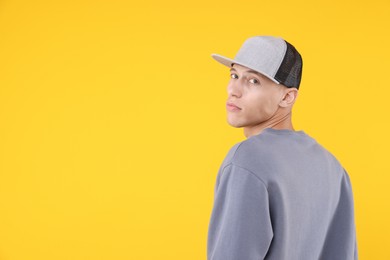 Photo of Young man wearing stylish baseball hat on yellow background, space for text