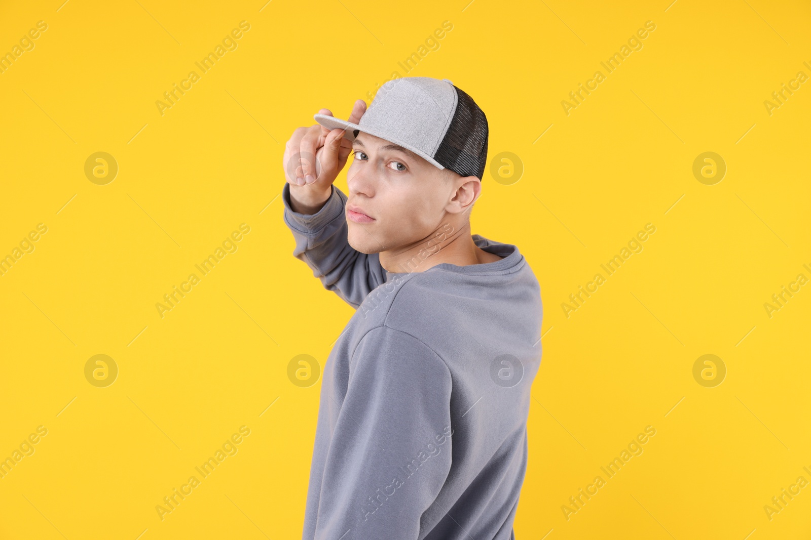 Young man wearing stylish baseball hat on yellow background Photo of Young man wearing stylish baseball hat on yellow background