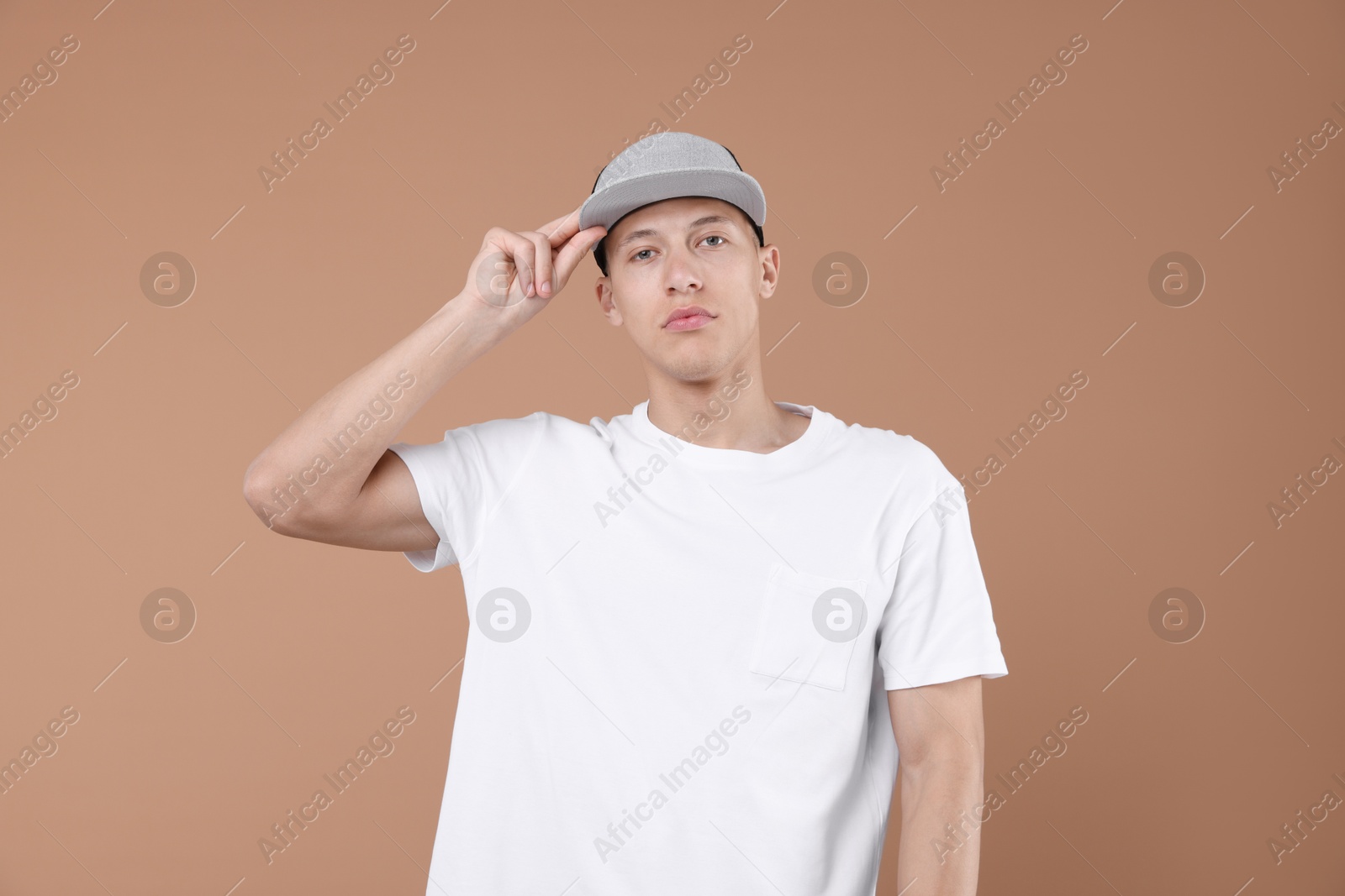 Young man wearing stylish baseball hat on light brown background Photo of Young man wearing stylish baseball hat on light brown background