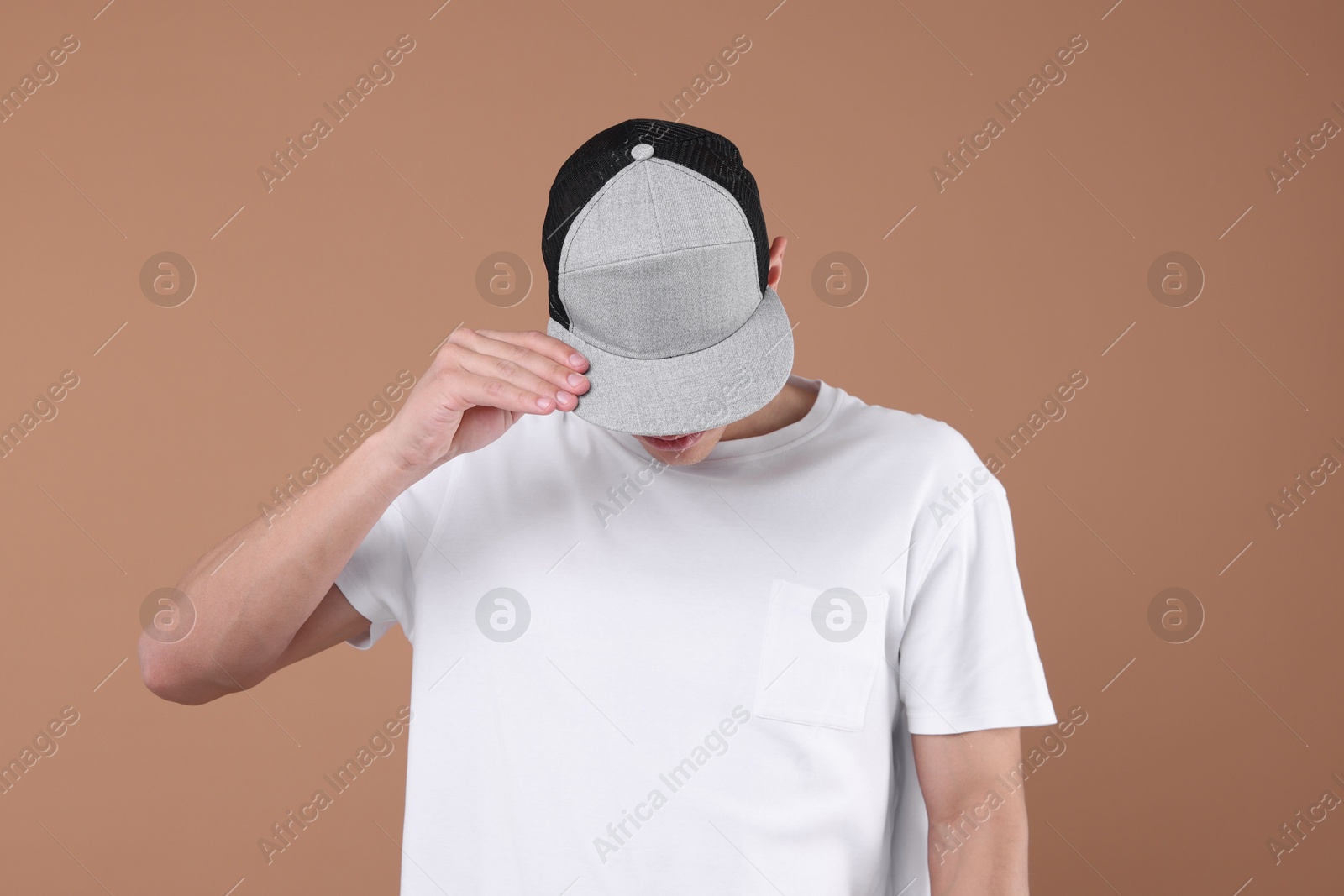 Young man wearing stylish baseball hat on light brown background Photo of Young man wearing stylish baseball hat on light brown background