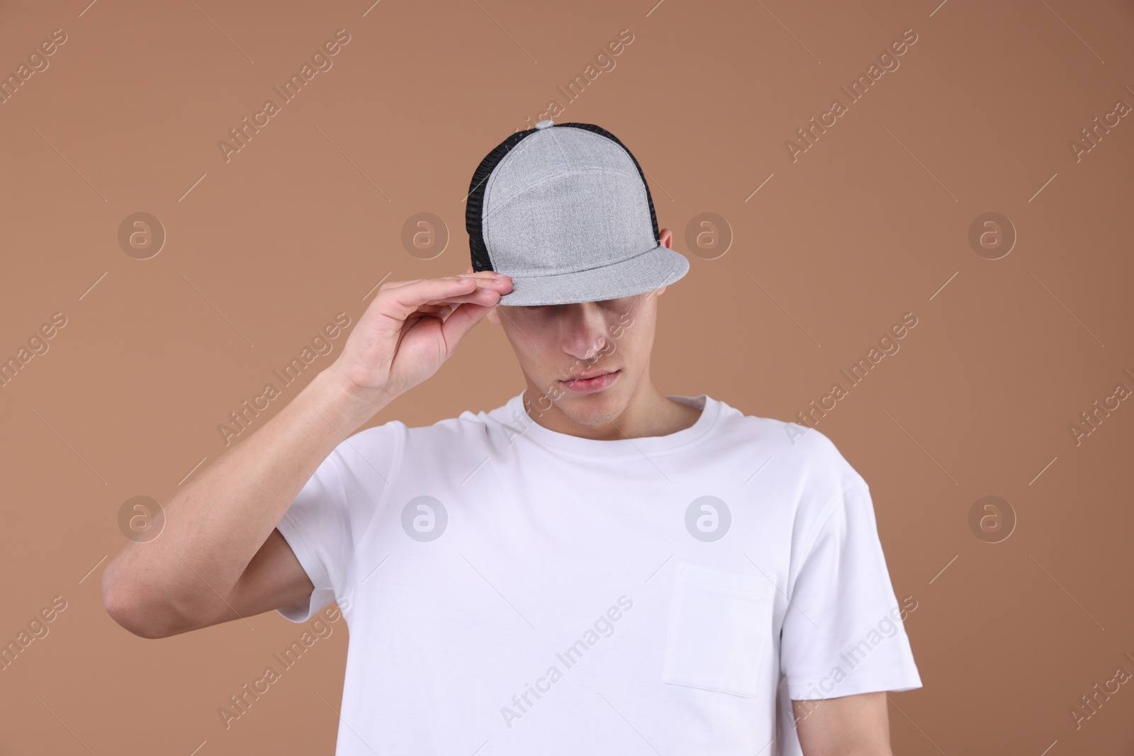 Young man wearing stylish baseball hat on light brown background Photo of Young man wearing stylish baseball hat on light brown background