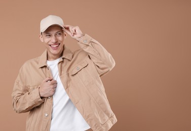 Photo of Young man wearing stylish beige baseball hat on light brown background, space for text