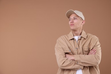 Photo of Young man wearing stylish beige baseball hat on light brown background, space for text
