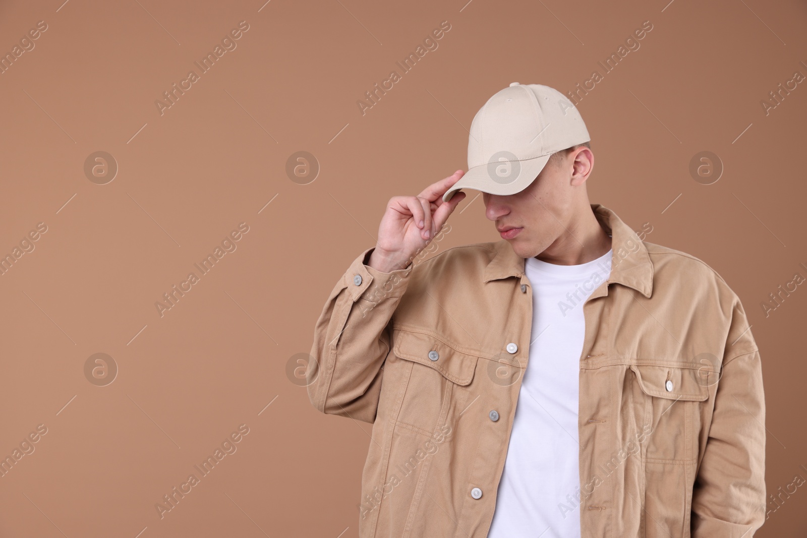 Young man wearing stylish beige baseball hat on light brown background, space for text Photo of Young man wearing stylish beige baseball hat on light brown background, space for text