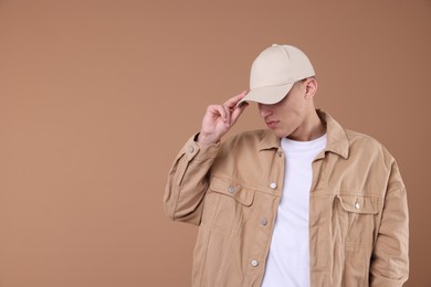 Photo of Young man wearing stylish beige baseball hat on light brown background, space for text